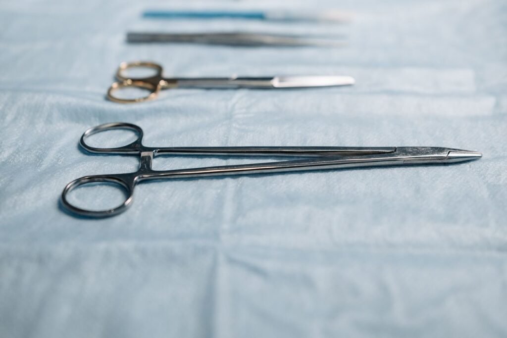 Close-up of surgical tools including a needle holder on a blue cloth in a medical setting.